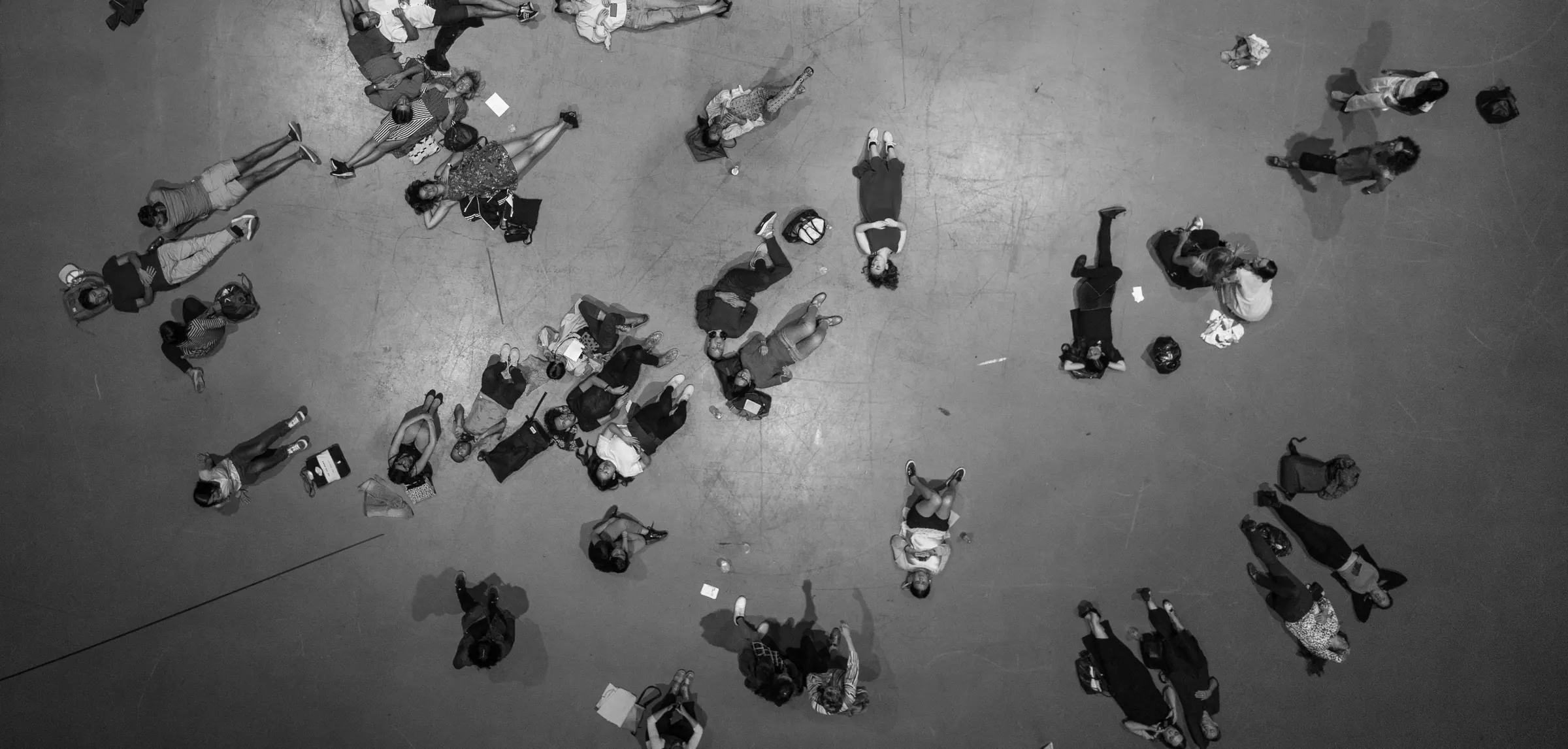 Overhead black-and-white photograph of people lying scattered across a concrete floor